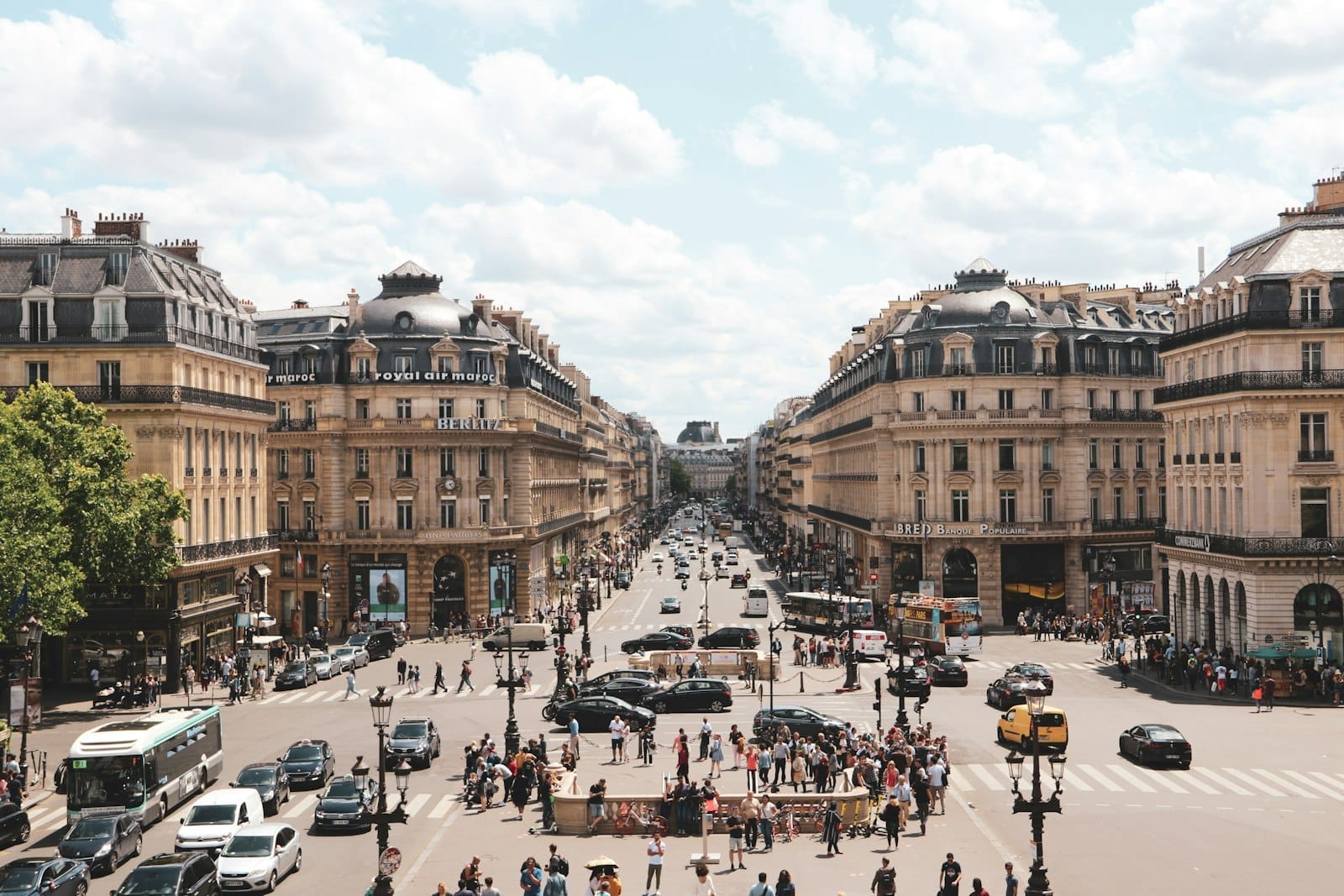 Vista panoramica dei Grands Boulevards di Parigi con i classici edifici haussmanniani, la vivace scena stradale, auto e pedoni sotto un cielo parzialmente nuvoloso.