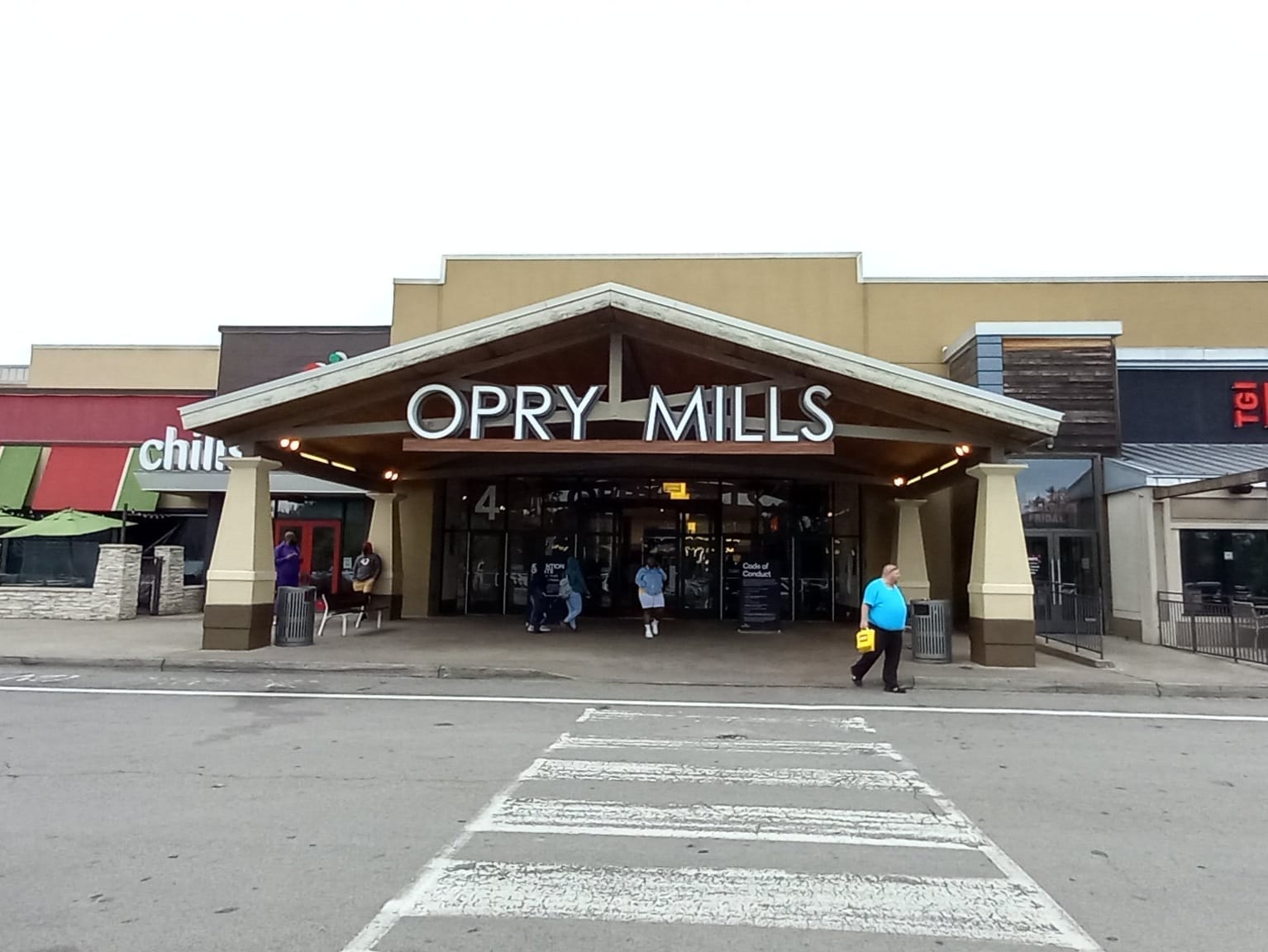 Entrada principal del centro comercial Opry Mills en Nashville con un gran letrero, entrada techada y personas caminando en un día nublado.