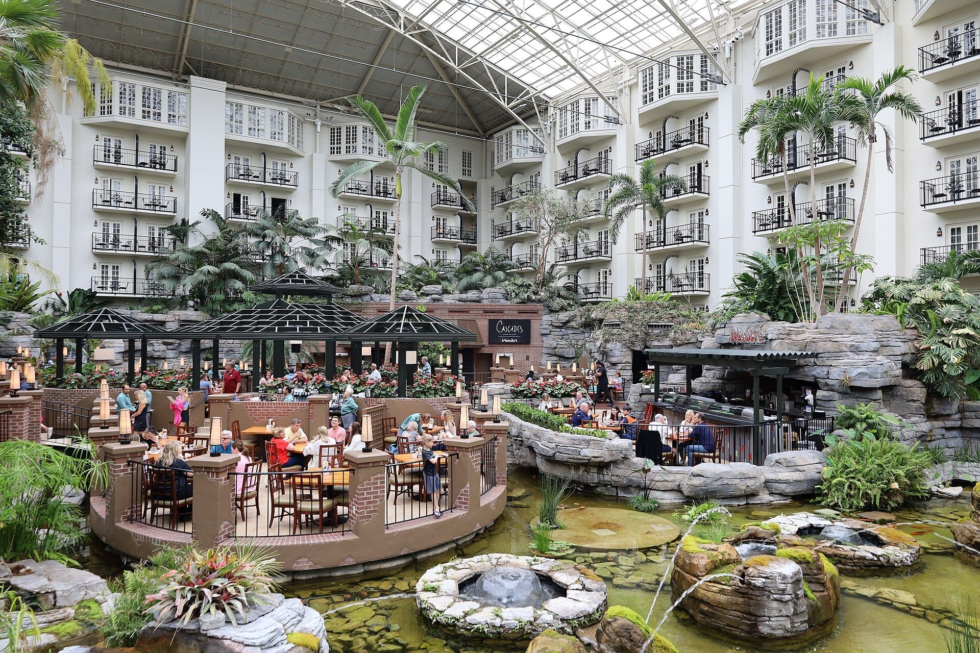 Amplio atrio del Gaylord Opryland Resort con terrazas para cenar, exuberantes plantas tropicales, fuentes de agua y balcones del hotel bajo un techo de cristal.