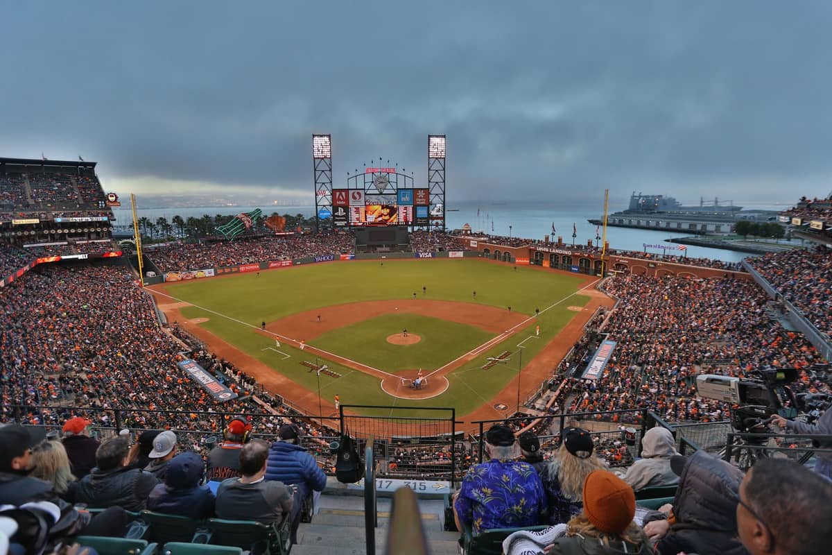 Vista panoramica di Oracle Park gremito di tifosi durante una partita di baseball, con il campo, il tabellone e la baia di San Francisco sullo sfondo.