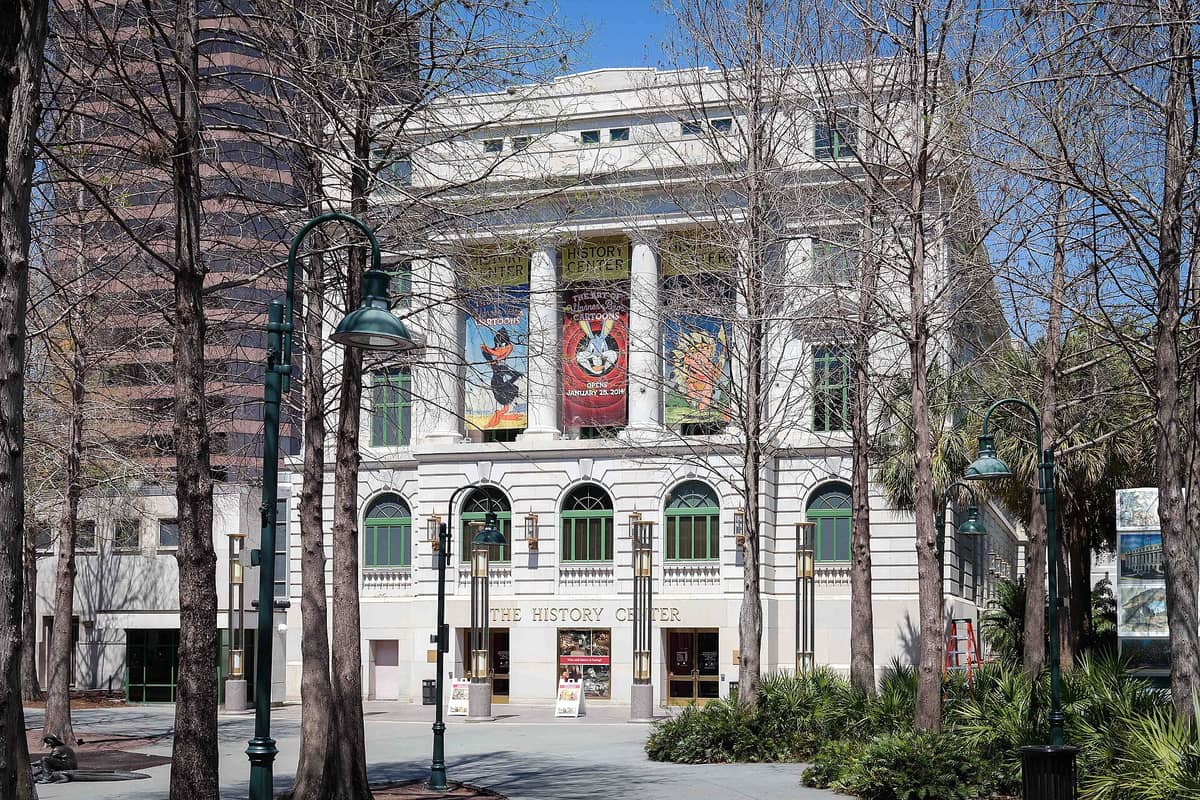 Front view of the Orange County Regional History Center in downtown Orlando, with banners, arched windows, and trees in the plaza.