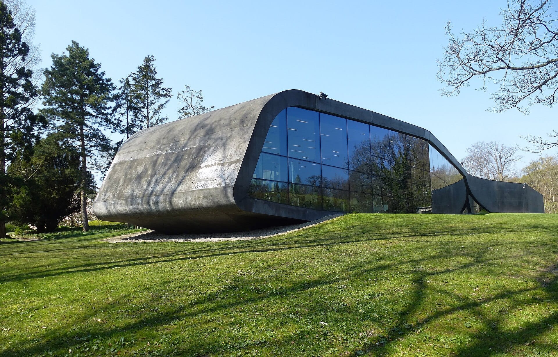 Moderna estensione progettata da Zaha Hadid al Museo Ordrupgaard di Copenaghen, con facciata curva in cemento e vetro circondata da prato verde e alberi.
