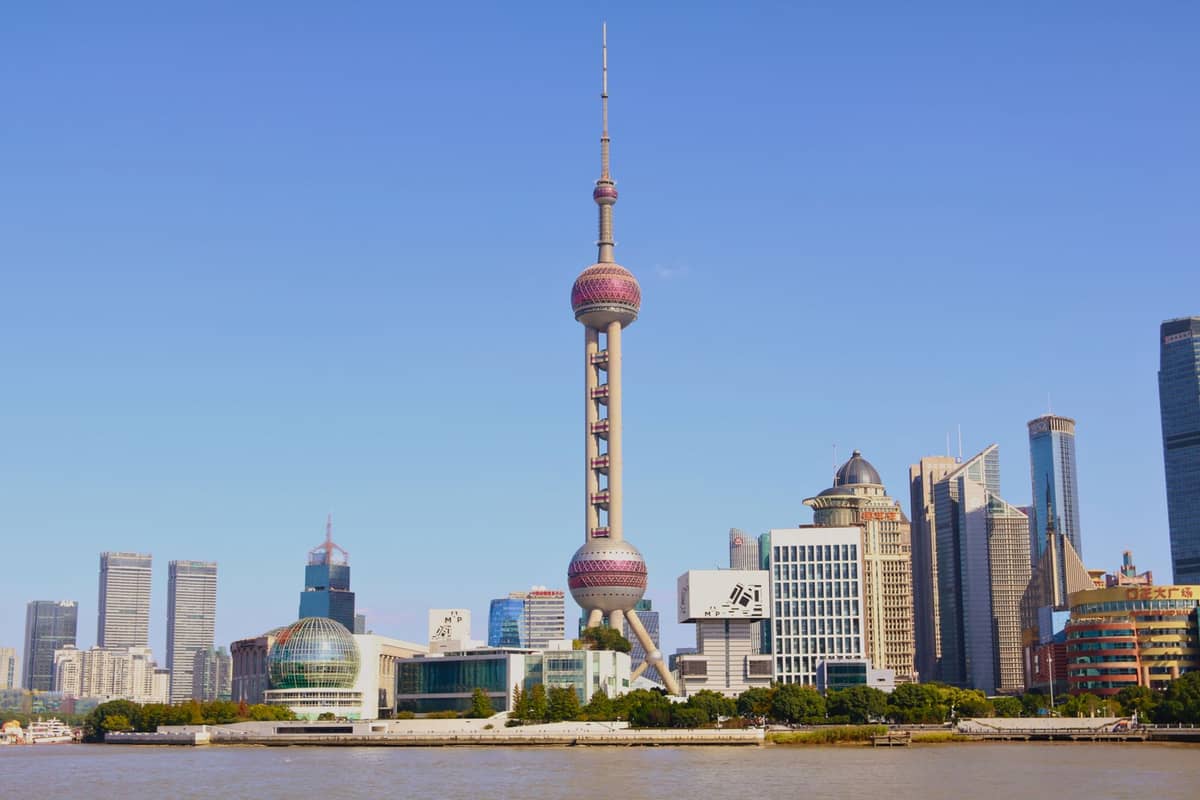 Der Oriental Pearl Radio & Television Tower in Shanghai ragt markant aus der Pudong-Skyline heraus, mit seinen rosafarbenen Leuchtkugeln, einem klaren blauen Himmel und modernen Wolkenkratzern ringsum.