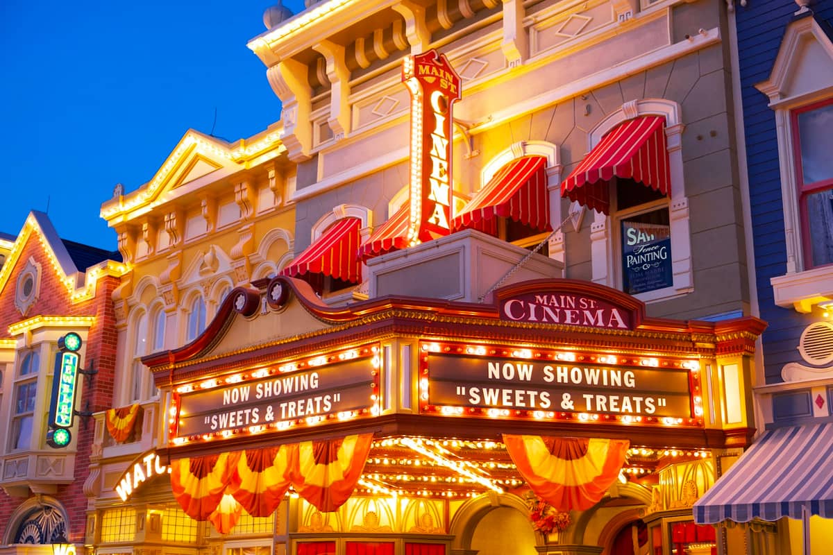 Nächtliche Aufnahme des beleuchteten Main Street Cinema Kinomärquees im Disney Magic Kingdom, festlich dekoriert mit bunten Lichtern.
