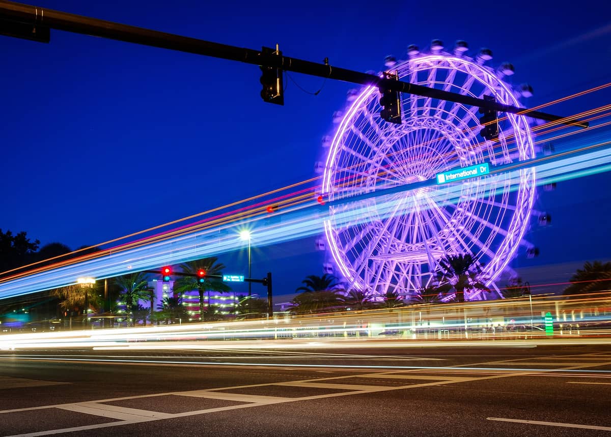 Blick auf das Riesenrad des ICON Park in Orlando bei Nacht, mit Lichtspuren von Autos, die im Vordergrund die Kreuzung am International Drive passieren.