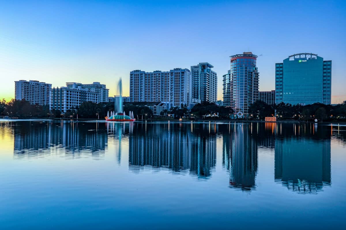 Orlando, Florida skyline with recognizable Lake Eola fountain and high-rise buildings reflected in the lake at sunset.