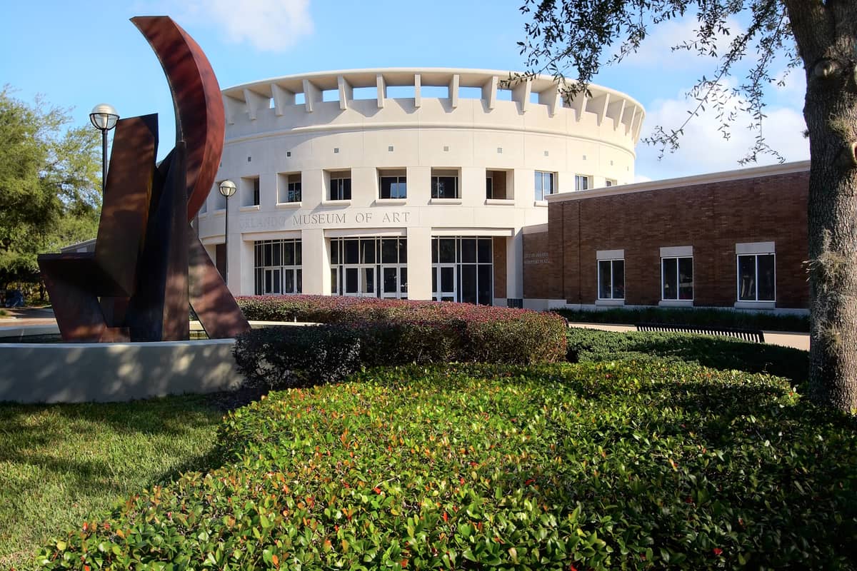 Exterior of the Orlando Museum of Art with its distinctive round entrance, modern sculpture, brick walls, and leafy green landscaping in Loch Haven Park.