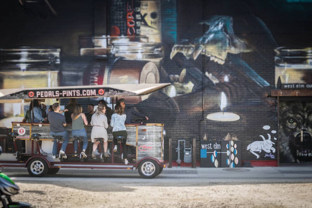 Gruppe von Menschen auf einem Pedal Pub an einer Wandmalerei vorbei, die das lokale Nachtleben und die Street-Art-Atmosphäre widerspiegelt.