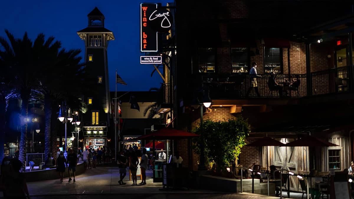 Night view of Orlando nightlife district with people walking, illuminated wine bar sign, palm trees, and lively street atmosphere.