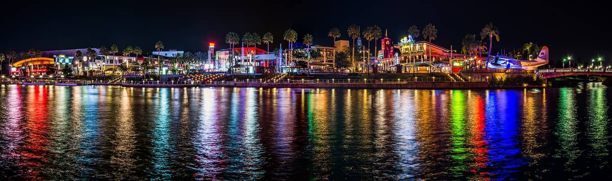 Panoramablick auf Universal CityWalk Orlando bei Nacht mit bunten Neonlichtern, die sich im Wasser spiegeln, und sichtbaren Palmen.