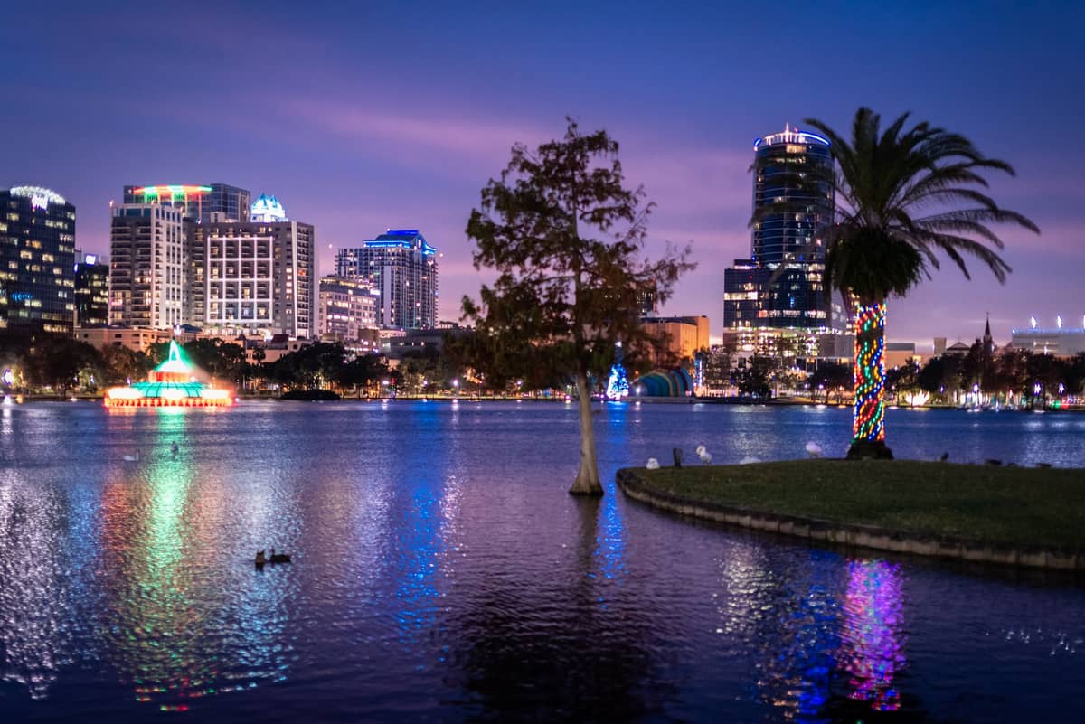 Lake Eola di notte con lo skyline di Orlando, una fontana illuminata, palme e riflessi sull'acqua, come attrazione gratuita nel centro della città.