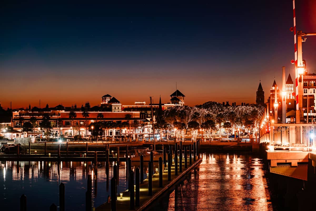 Una animada zona frente al agua, bien iluminada por la noche, con luces de colores que se reflejan en el agua, con edificios probablemente de una zona turística de Orlando.