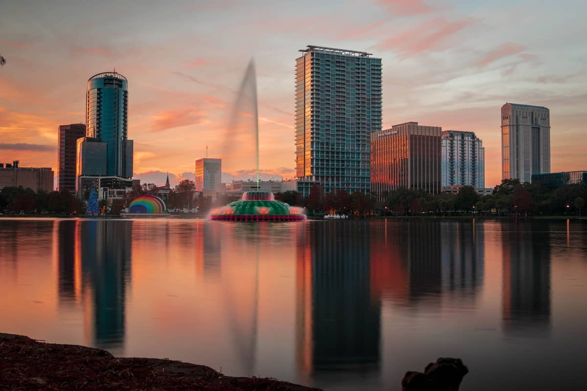 Horizonte de Orlando y rascacielos reflejados en el Lake Eola al atardecer, con una gran fuente salpicando agua y un cielo parcialmente nublado.