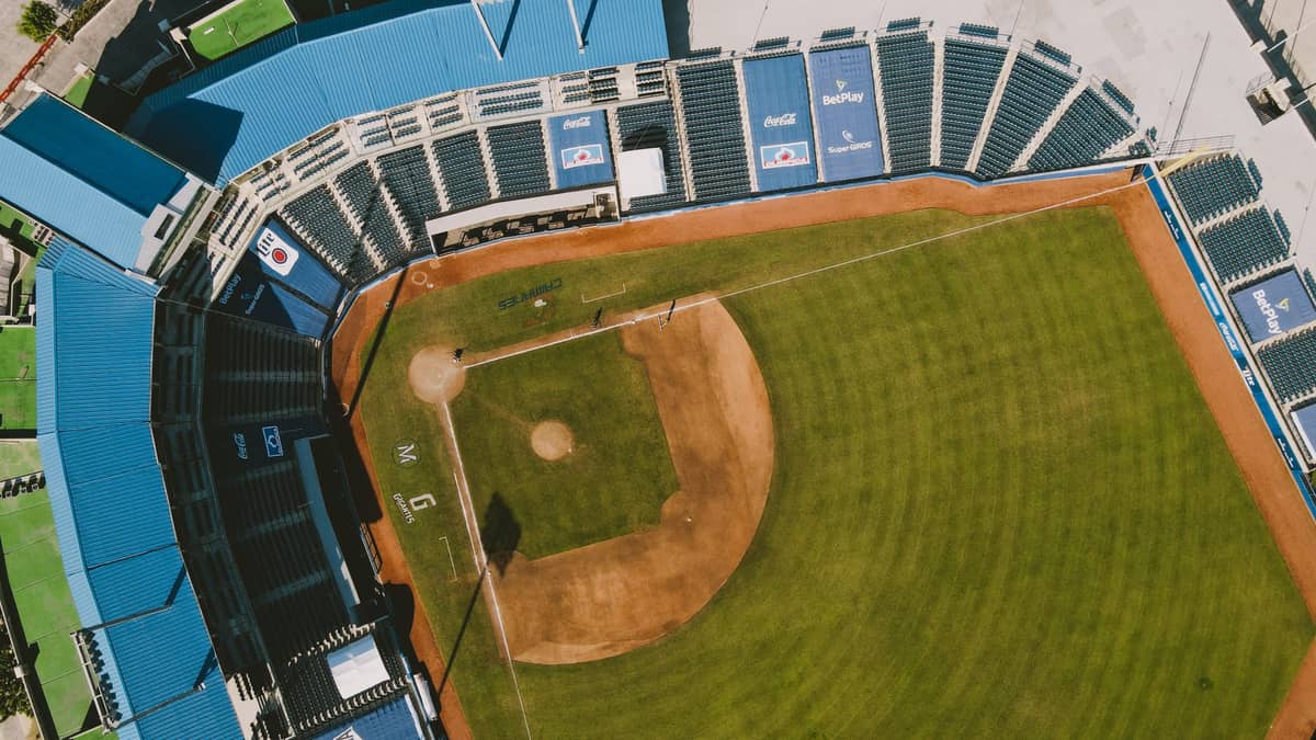 Aerial view of a baseball stadium with green field and blue seating, showing the entire infield and stands under daylight.