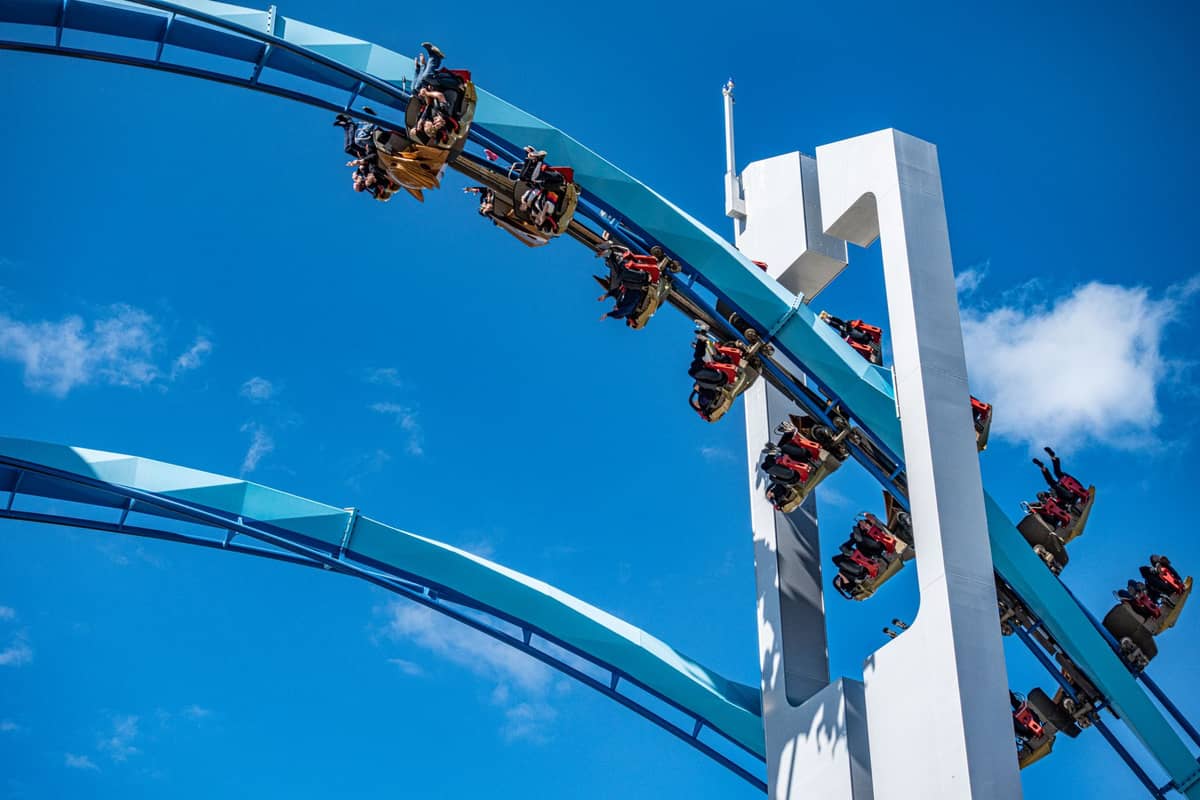 Nahaufnahme einer blauen Achterbahn mit auf dem Kopf stehenden Fahrgästen vor einem klaren blauen Himmel, typisch für die Achterbahnattraktionen von SeaWorld Orlando.