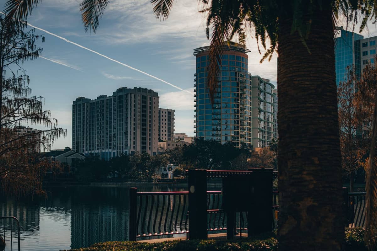 Vue sur un lac vers les immeubles modernes du centre-ville d'Orlando, avec une rambarde et un palmier au premier plan.