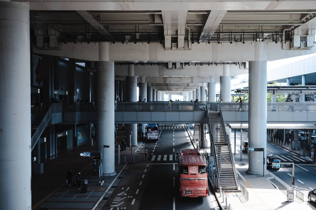 The exterior arrival and departure area at one of Osaka’s airports, with buses, pillars, and overhead walkways under the terminal building.