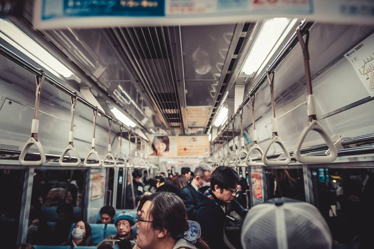 Interior of a Japanese metro train with passengers, hanging straps, and signage in Japanese, typical of Osaka public transit.