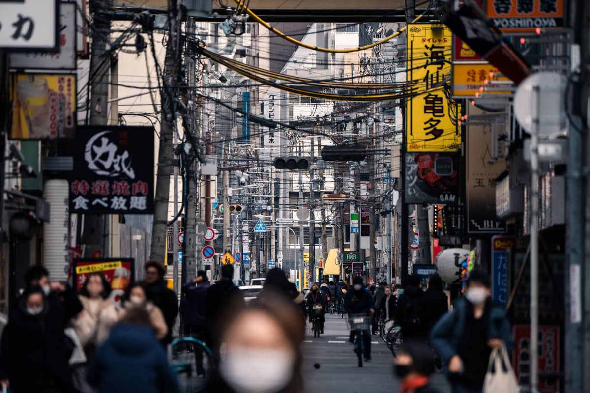 Busy Osaka street with Japanese signs, overhead cables, people walking and cycling, urban cityscape atmosphere.