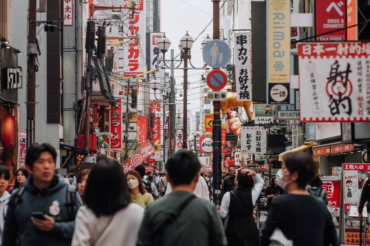 Crowds of people walking along a busy street in Osaka lined with colorful shop signs and banners.