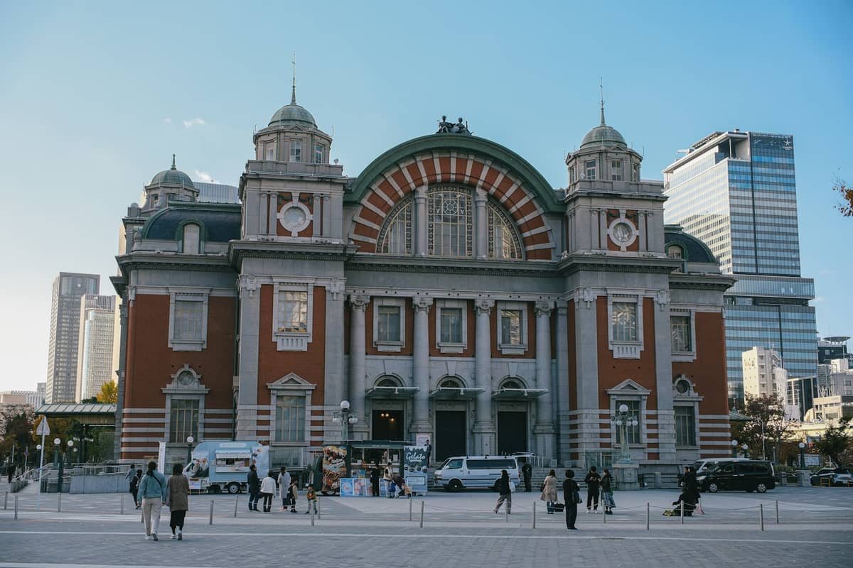 Facade of Osaka City Central Public Hall with its ornate Neo-Renaissance architecture, red brick and white stone accents, and people walking in the plaza.