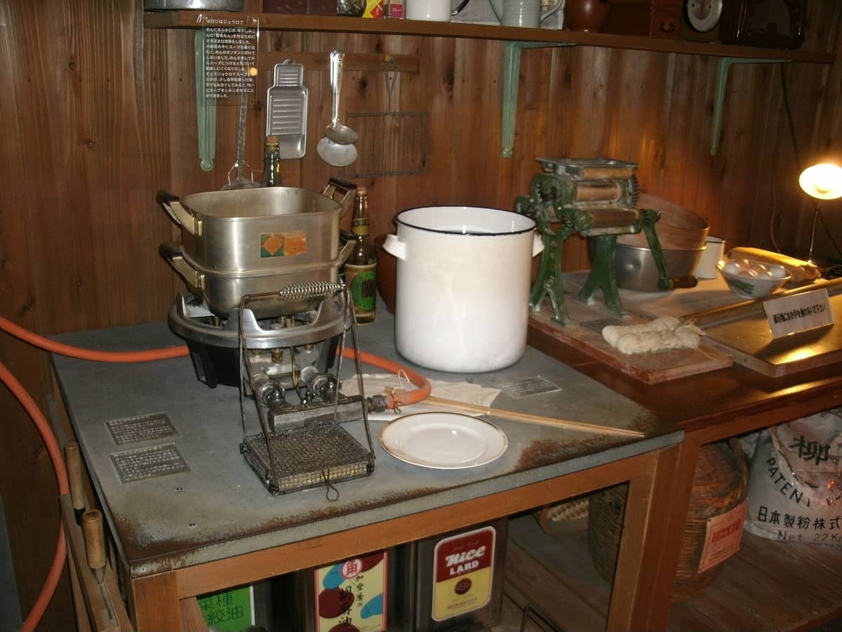 Exhibit of vintage noodle-making equipment and kitchen tools displayed in a museum setting with Japanese signage