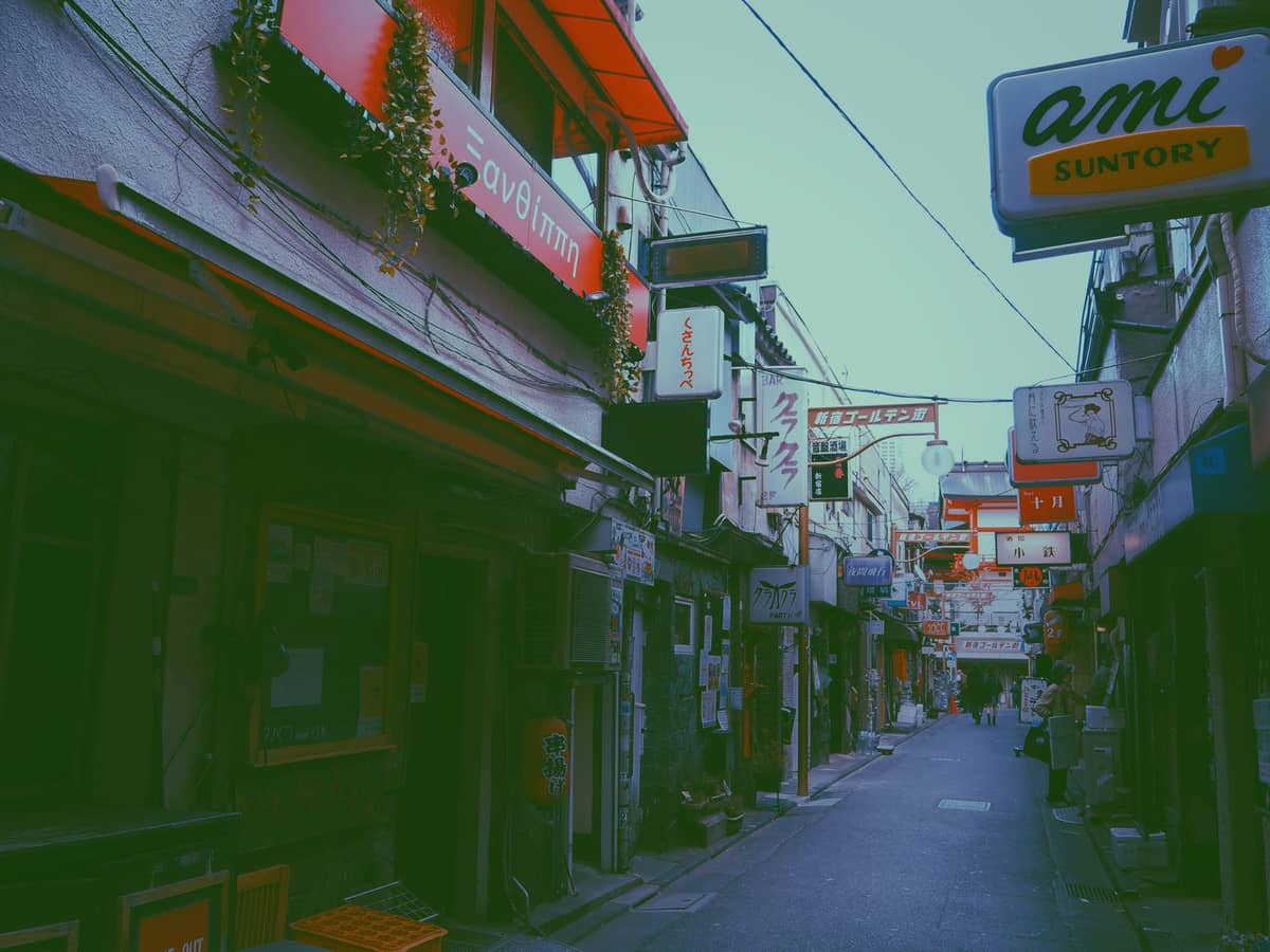 Narrow, retro alleyway lined with small bars and vintage signs in an old Osaka neighborhood in daylight.
