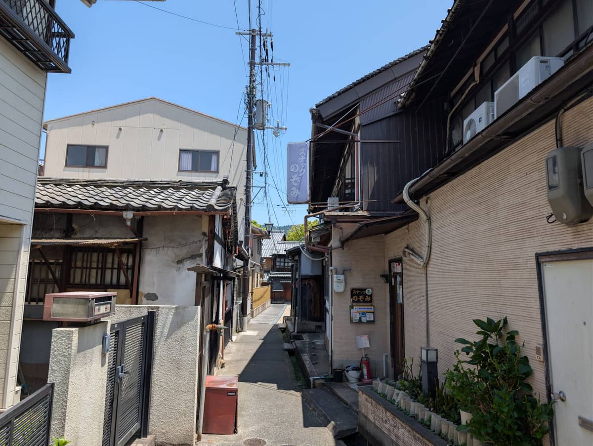 Narrow residential lane in Osaka's Nakazakicho neighborhood with traditional wooden houses and overhead power lines on a sunny day.