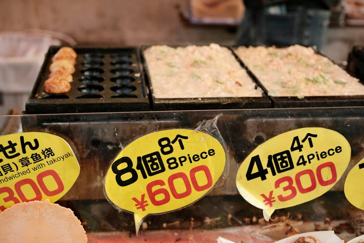 Close-up of takoyaki being cooked with clear price signs for 8 and 4 pieces at a food stall in Osaka.