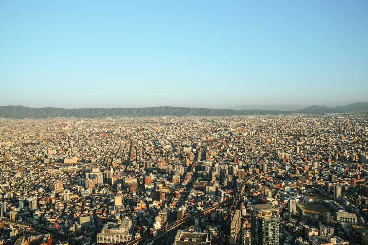 Wide aerial view of Osaka cityscape with densely packed buildings and distant mountains under a clear blue sky