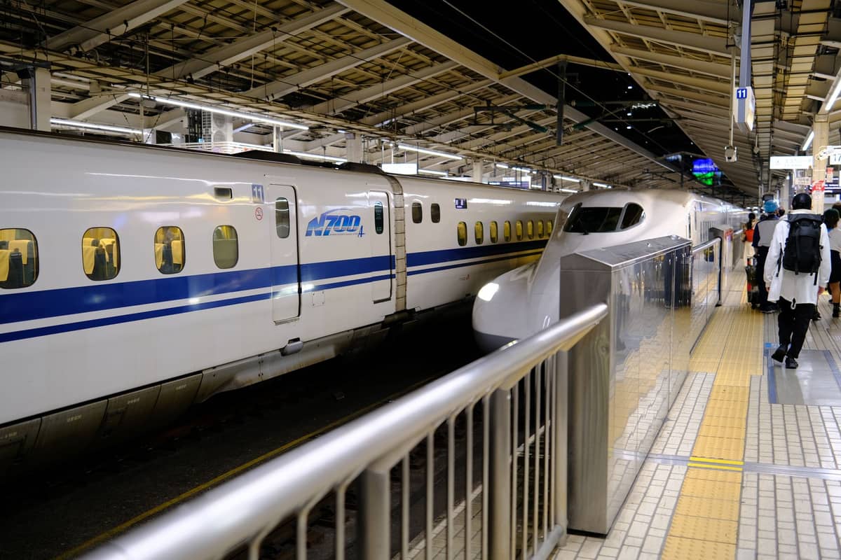 Two Shinkansen bullet trains at a platform in a modern Japanese train station with passengers walking nearby.