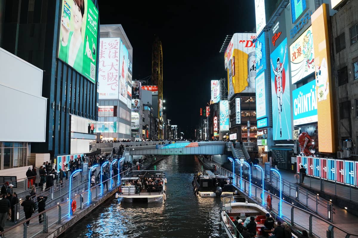 Dotonbori canal at night with neon-lit buildings, bright billboards, and crowds along the waterfront in Osaka's famous street food district.