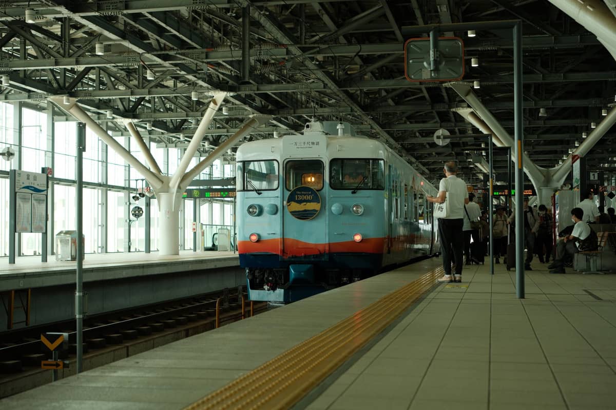 A modern train stopped at an indoor platform in Japan with passengers waiting, representing travel between Osaka and Kyoto by rail.