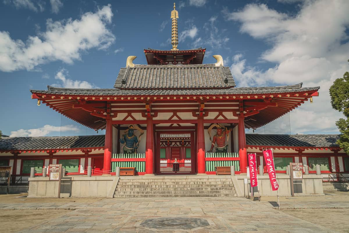 Front view of Shitennoji Temple's main gate in Osaka with guardian statues, traditional architecture, and blue sky.