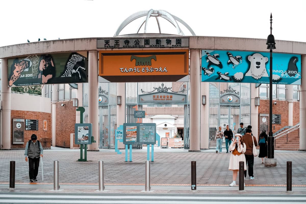 Front entrance of Tennoji Zoo in Osaka, with colorful animal signs, people walking, and a distinctive domed gate structure.