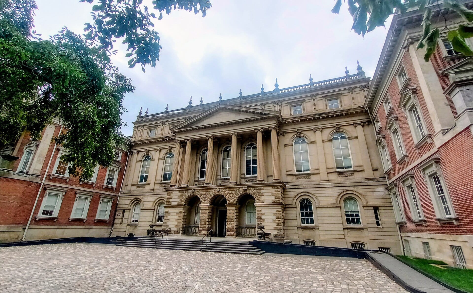 ภาพด้านหน้าของอาคาร Osgoode Hall สไตล์นีโอคลาสสิกอันยิ่งใหญ่ พร้อมเสาหิน ทางเข้าโค้งโอ้อ่า และปีกอาคารอิฐแดงในวันที่มีเมฆปกคลุม