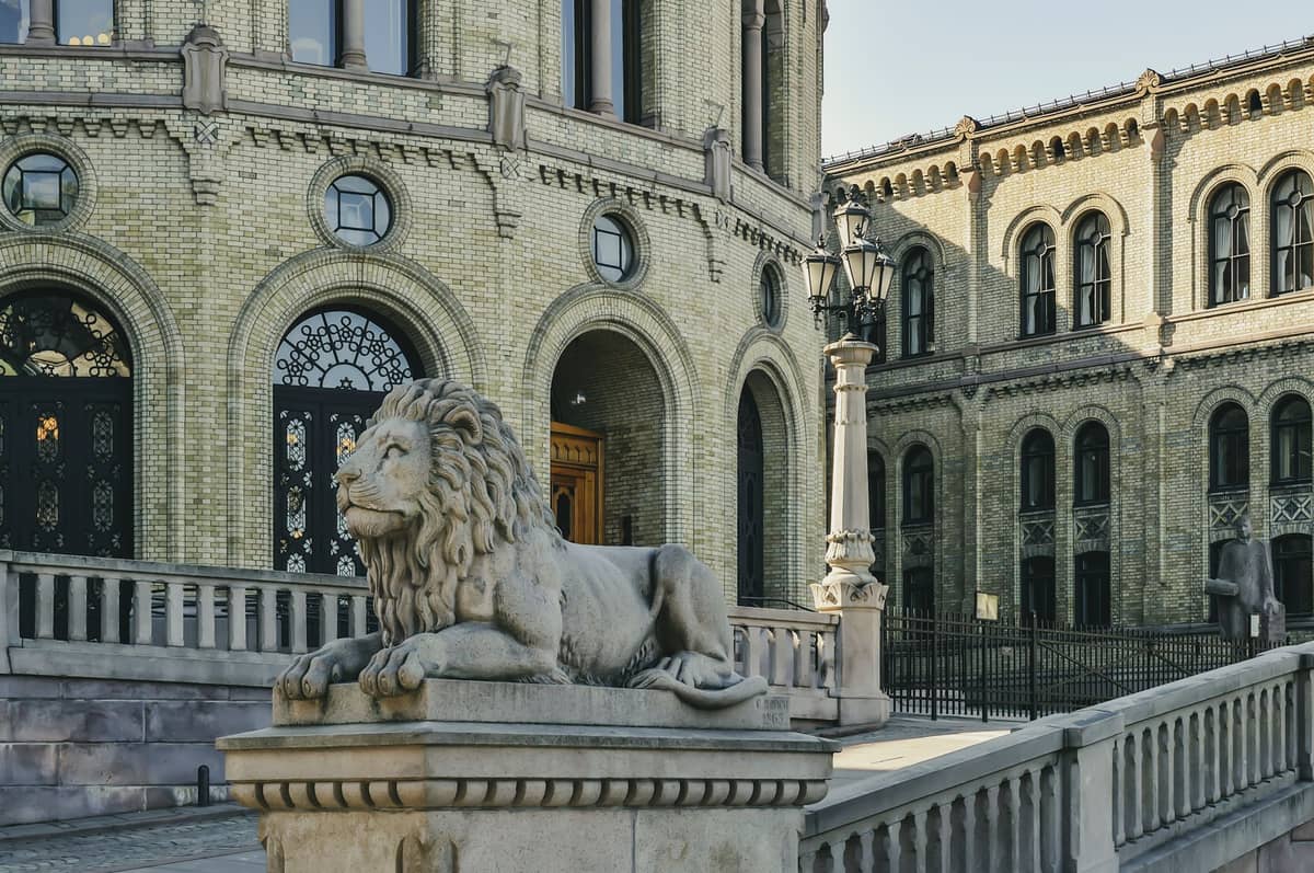 วิวอาคารรัฐสภาประวัติศาสตร์ Stortinget ในออสโล พร้อมซุ้มโค้งอิฐสีเหลืองอันโดดเด่นและประติมากรรมสิงโตหินด้านหน้า
