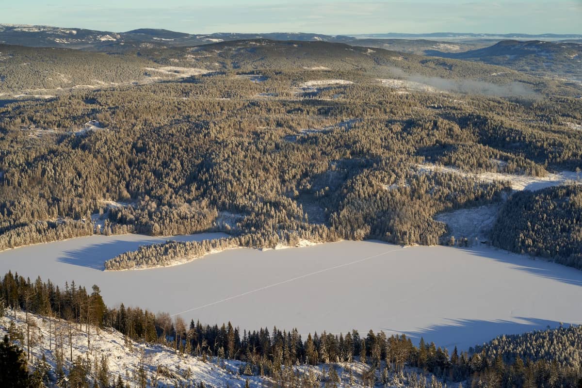 วิวพาโนราม่าในฤดูหนาวของป่า Nordmarka ใกล้ออสโล ประเทศนอร์เวย์ เห็นทะเลสาบน้ำแข็งล้อมรอบด้วยเนินเขาที่เต็มไปด้วยต้นไม้ ภายใต้ท้องฟ้าแจ่มใส