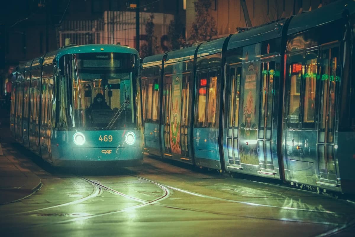 รถรางสีน้ำเงินของ Oslo ยามค่ำคืนพร้อมผู้โดยสารภายใน เห็นที่สถานีพร้อมแสงไฟของเมืองสะท้อนบนพื้นถนนที่เปียก