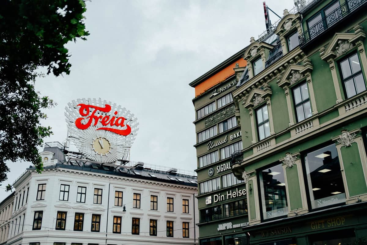 Karl Johans gate ที่มีประวัติศาสตร์ในออสโลพร้อมป้าย Freia อันโด่งดังและหน้าร้านคลาสสิกในวันที่มีเมฆมาก