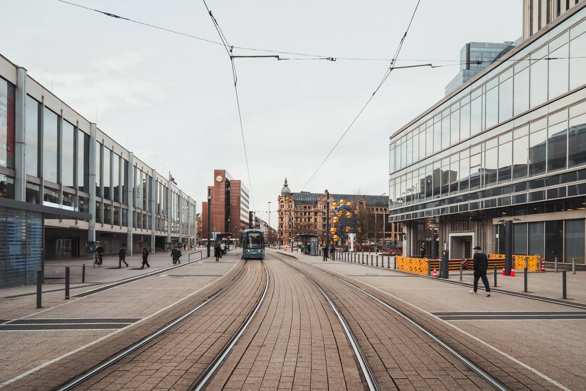 วิวรางรถรางและรถรางด้านนอก Oslo Central Station พร้อมอาคารสมัยใหม่และผู้คนบริเวณใกล้เคียงในวันที่มีเมฆมาก