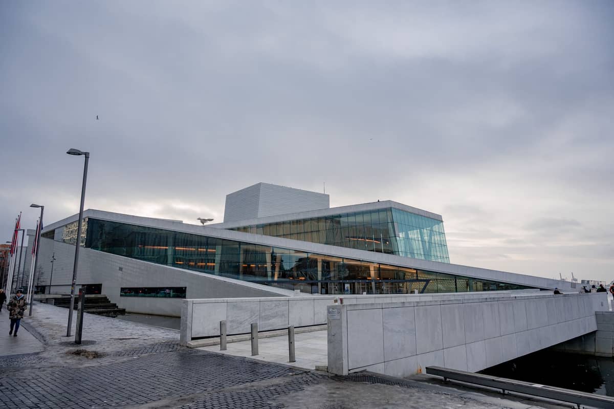 วิวกว้างของ Oslo Opera House พร้อมหลังคาเอียง ด้านหน้ากระจก และผู้คนเดินอยู่บริเวณริมน้ำในออสโล