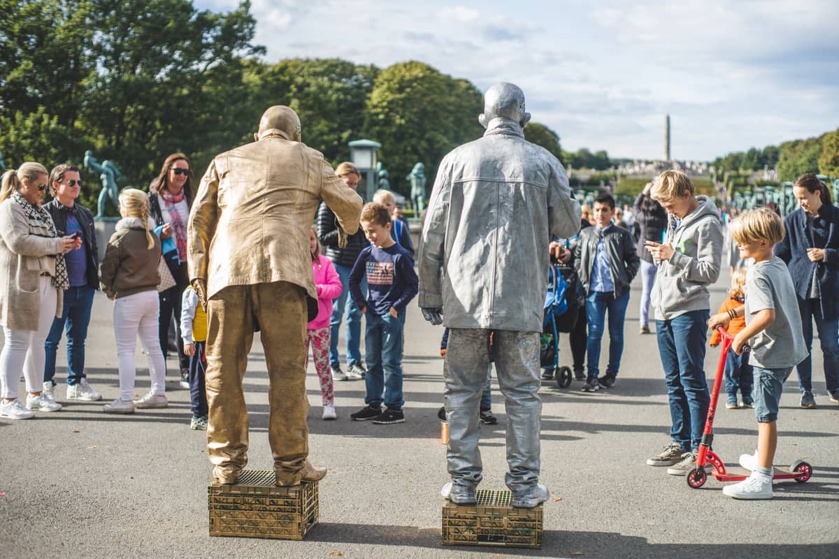 เด็กและครอบครัวชมการแสดงริมถนนที่สวนประติมากรรม Vigeland ในออสโล บรรยากาศครึกครื้น เต็มไปด้วยรูปปั้นและเด็กๆ ขี่สกู๊ตเตอร์