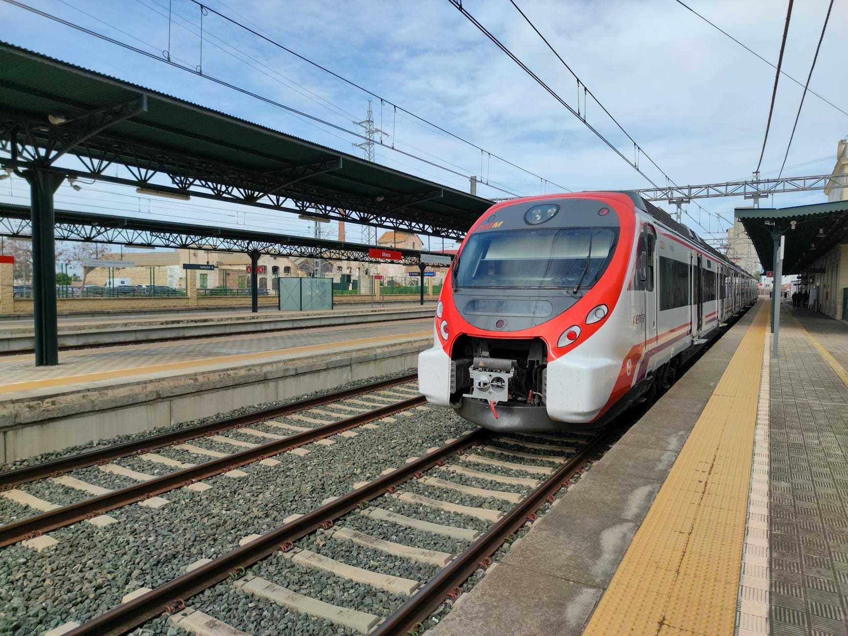 Modern regional train waiting at an outdoor platform under a blue sky, with station infrastructure visible around the tracks.