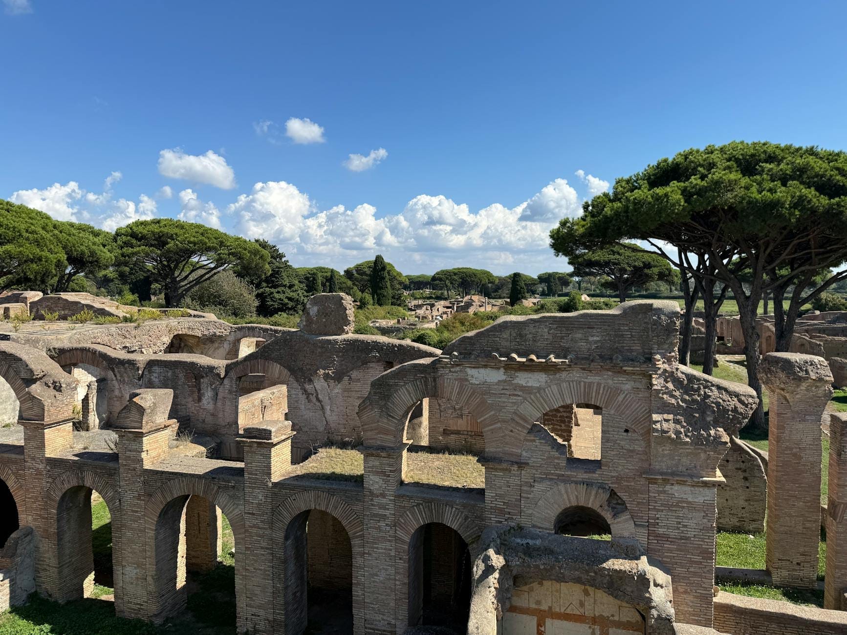 Panoramic view of Ostia Antica ruins with arched brick structures and umbrella pines under a blue sky.