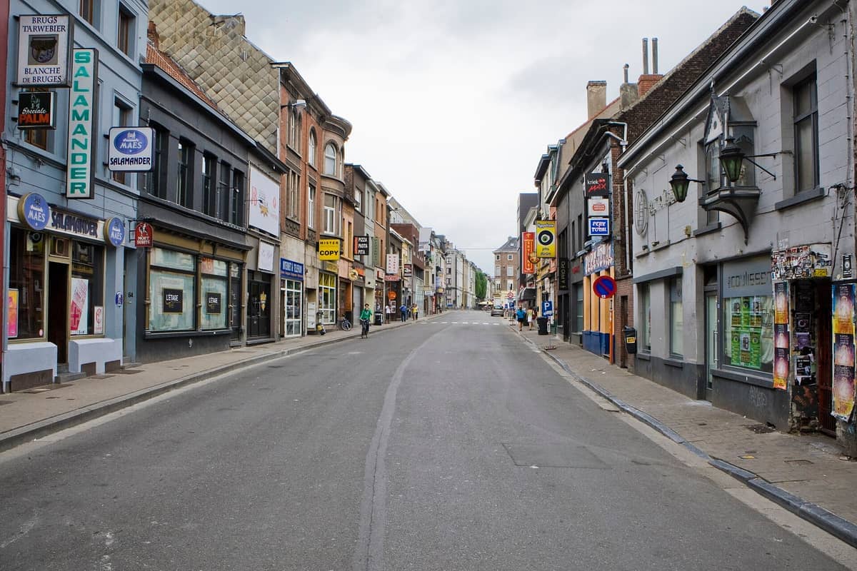 Wide view of Overpoortstraat in Ghent, lined with bars, restaurants, and colorful signs on a quiet, cloudy day.