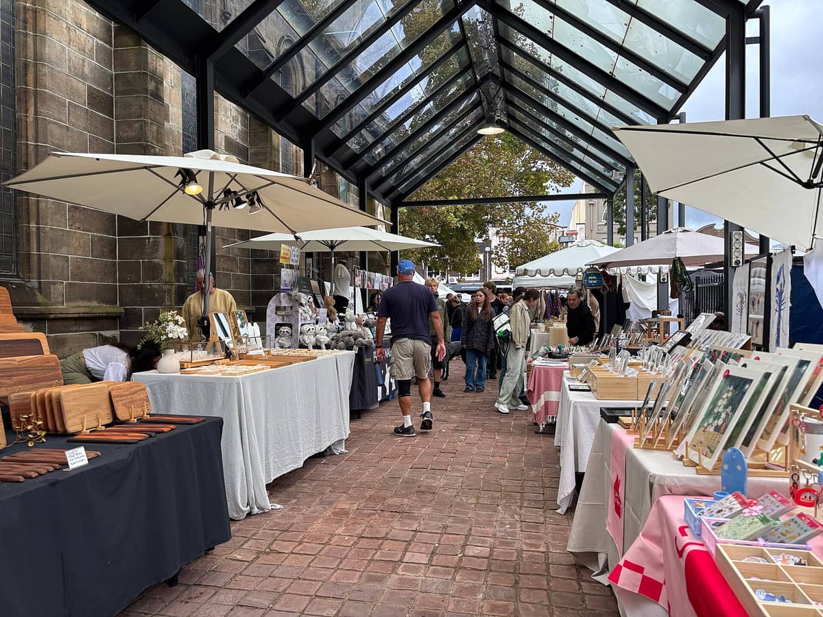 Stragany ze sztuką użytkową i innymi towarami pod parasolami wzdłuż ceglanej ścieżki obok kościoła Paddington Uniting Church na targu Paddington Markets w Sydney.