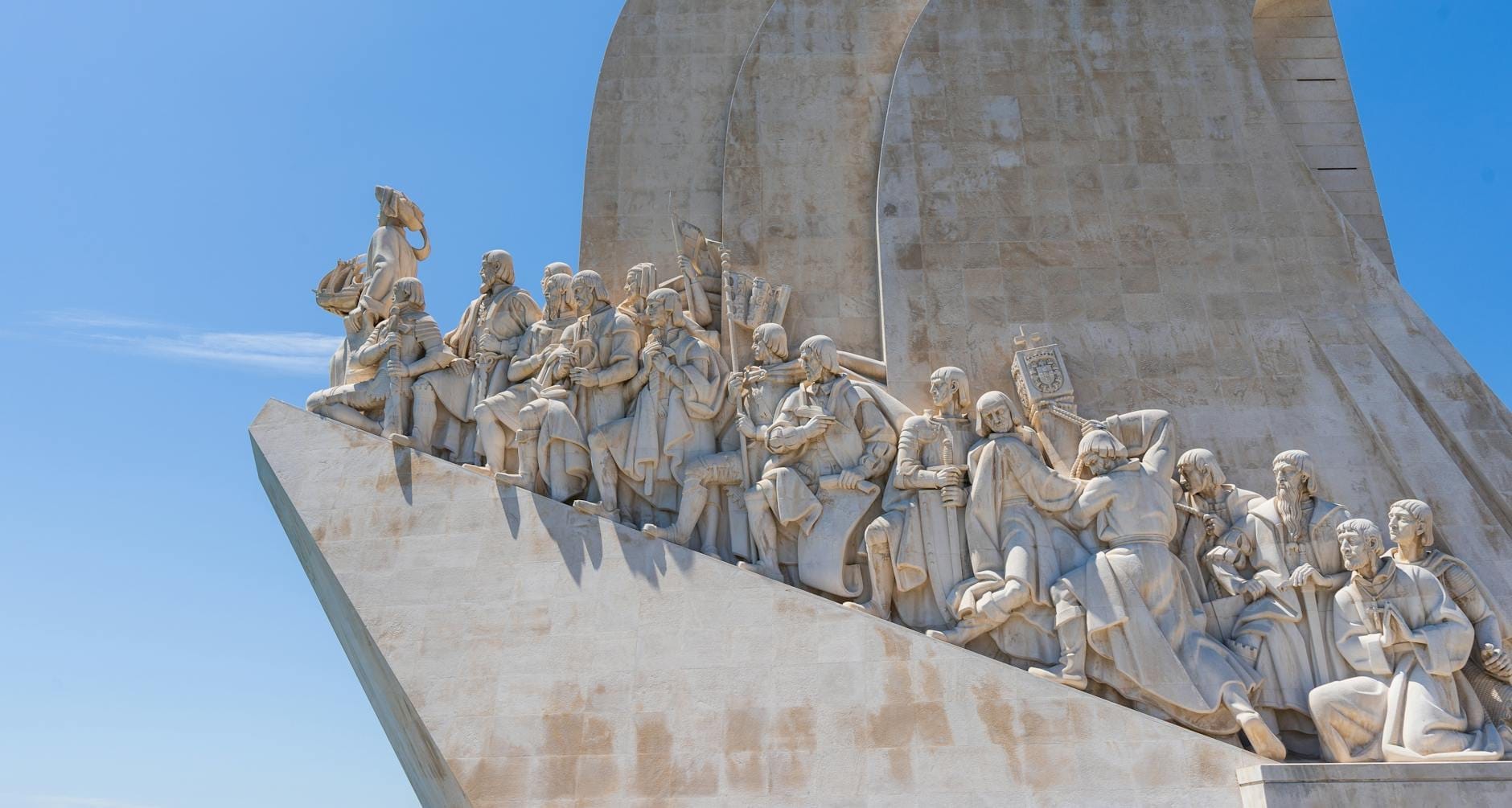Vista grandangolare del Padrão dos Descobrimentos a Lisbona, con le figure in pietra scolpita su sfondo di cielo blu, ideale come immagine di copertina per un'attrazione turistica.