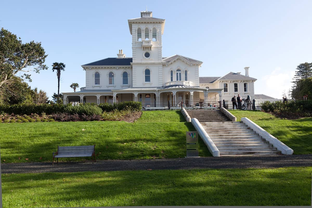 Frontansicht des Pah Homestead, einer viktorianischen Italianate-Villa in Auckland, mit breiter Treppe, gepflegtem Rasen und einigen Besuchern am Eingang.