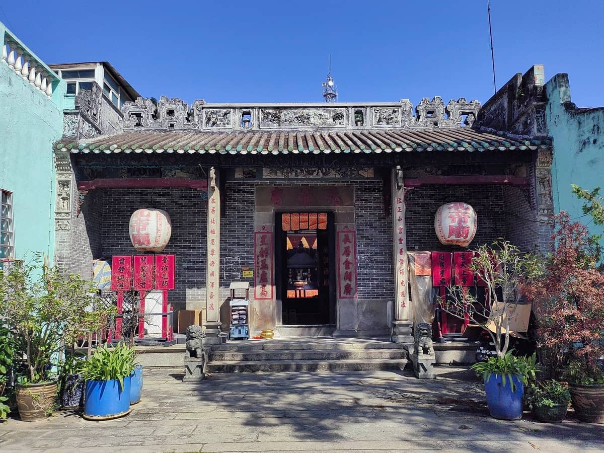 Tagesansicht des Pak-Tai-Tempels in Taipa, Macau, mit historischer Fassade, Steinstufen, roten Laternen und Topfpflanzen unter klarem blauen Himmel.